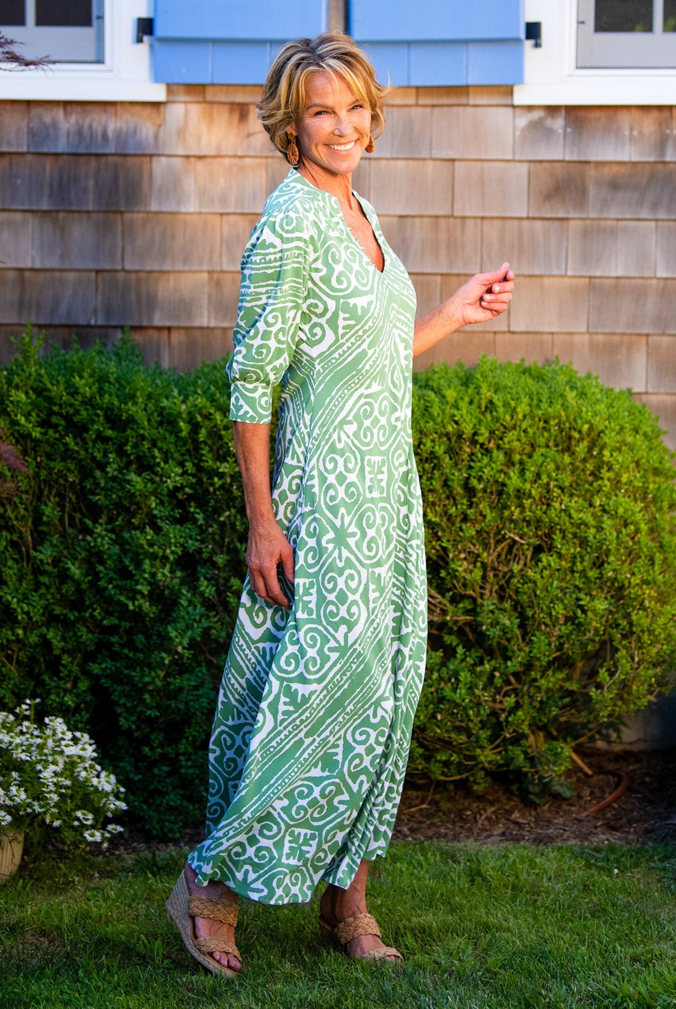 Woman in a green dress standing in front of a wooden building with blue shutters.